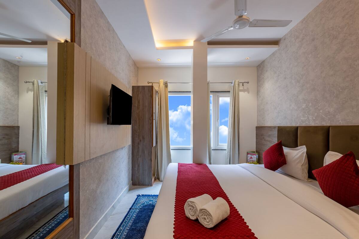 A hotel room with a large bed, a TV, a ceiling fan, and a view of the sky.