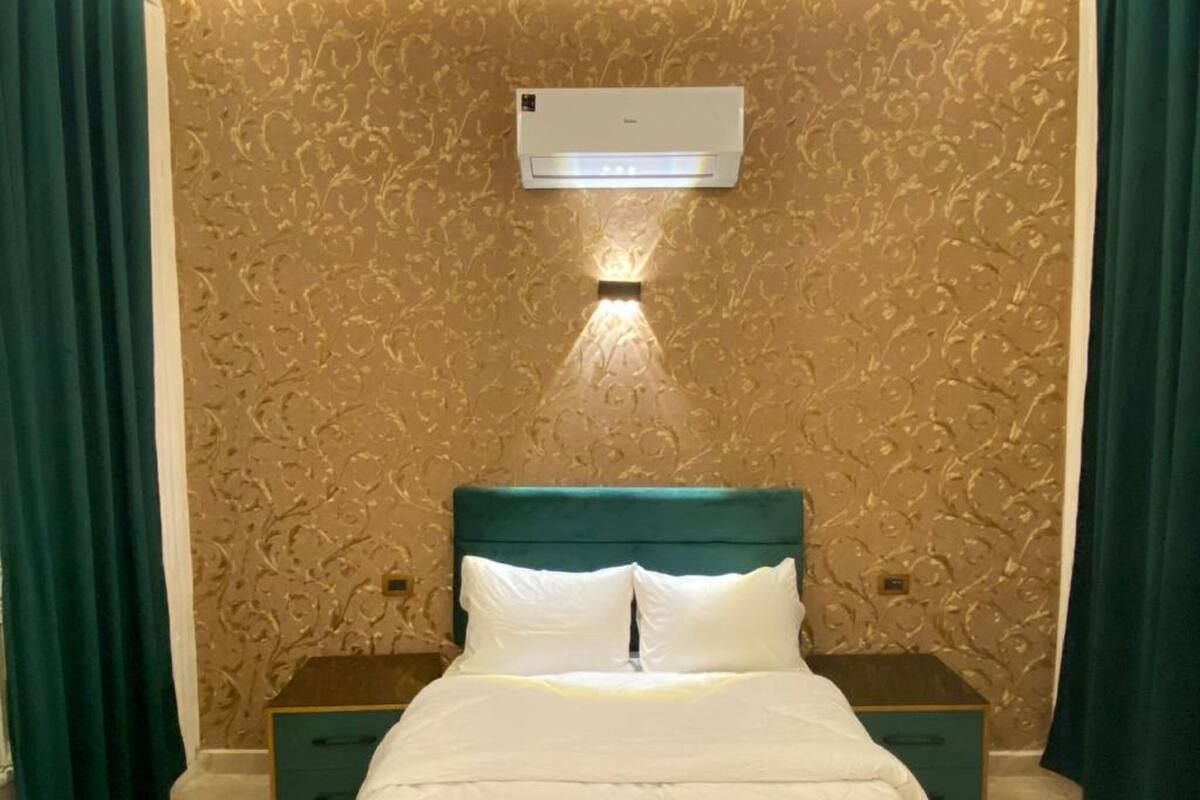 A neatly made bed with white bedding, a teal headboard, and two bedside tables with green drawers.
