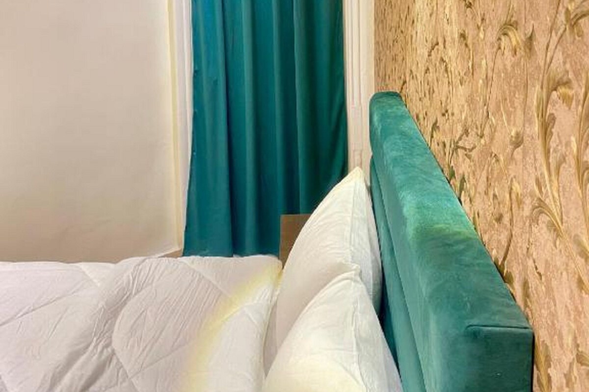 Habitación de hotel con cama, cortinas color turquesa, pared estampada y lámpara fijada a la pared.