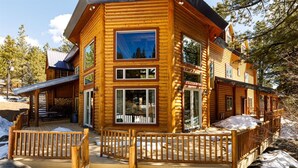 A log cabin with a deck, large windows, and a view of the surrounding forest.