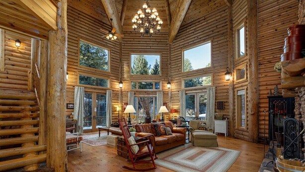 A log cabin interior with a fireplace, large windows, and a cozy seating area.
