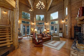 Interior de una cabaña de madera con chimenea, ventanas amplias y un rincón de estar acogedor.