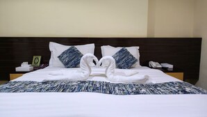 Un lit bien fait, avec du linge de lit blanc, deux serviettes décoratives en forme de cygne et une couvre-lit à motifs.