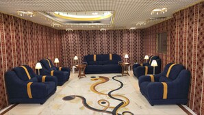 Une pièce avec un papier peint à motifs, un canapé bleu et des fauteuils assortis. On y trouve deux tables d’appoint avec des lampes.