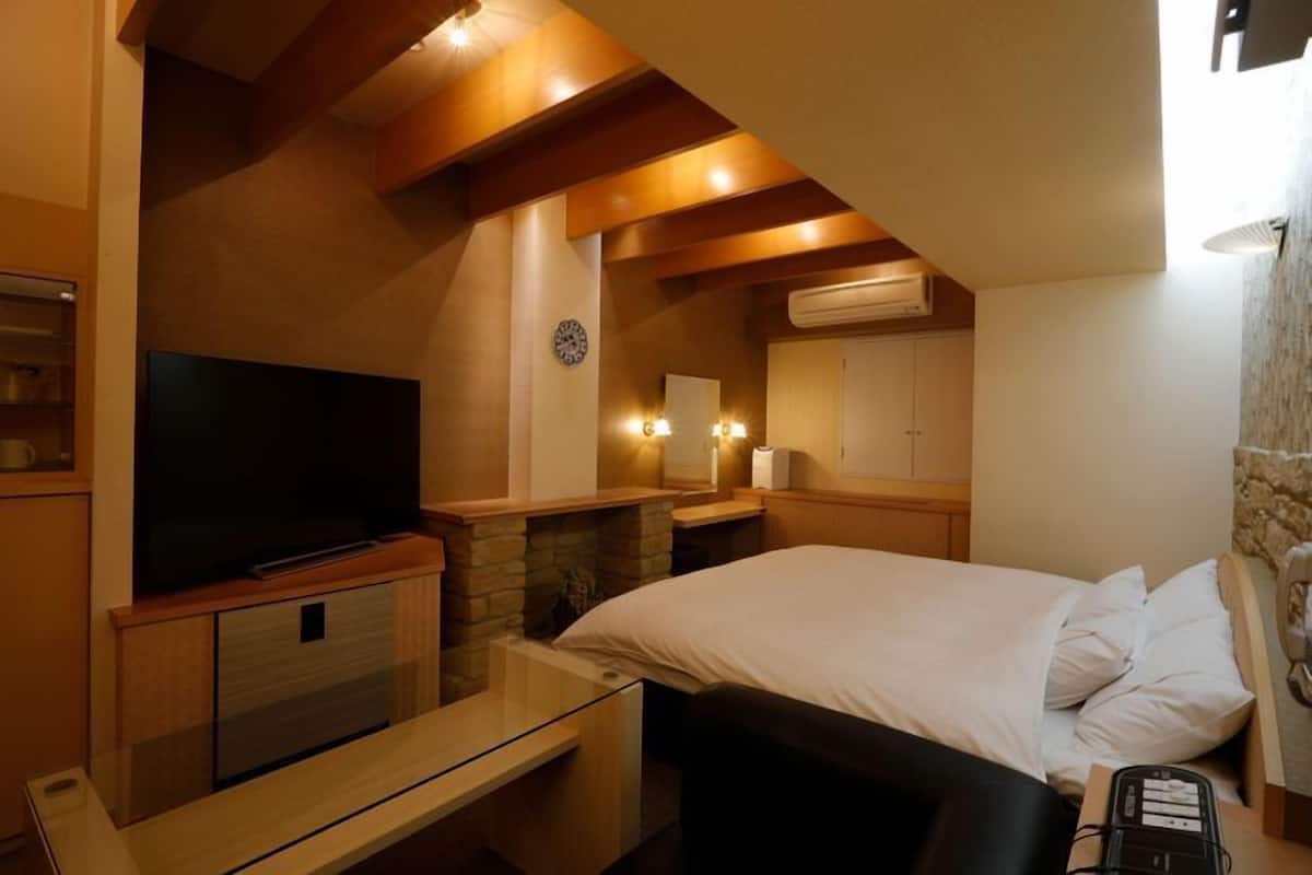 Habitación de hotel con televisor de pantalla plana, chimenea de piedra, cama con ropa blanca, mesita de noche y teléfono.