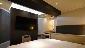 A modern hotel room with a large bed, a flat-screen TV mounted on the wall, and a small desk with a lamp. - HOTEL ROYALTON (Nagoya)