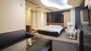 A modern hotel room with a large bed, a massage chair, a flat-screen TV, and a glass table. - HOTEL ROYALTON (Nagoya)