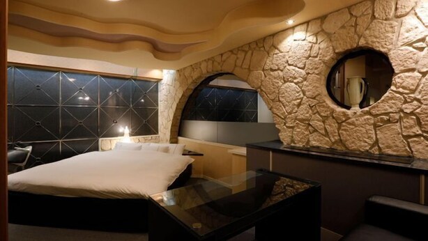 A modern bedroom with a large bed, a glass coffee table, and a stone accent wall with a circular mirror. - HOTEL ROYALTON (Nagoya)