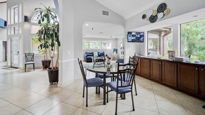 A spacious kitchen with a dining area, a large potted plant, and a view of the outdoors. - Bradenton Beach Condo -2 Pools- 15 minutes to Anna Maria Island Beaches-First Floor- End Unit (Bradenton)