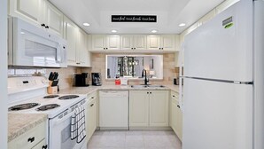 A modern kitchen with white cabinets, a microwave, stove, and refrigerator. There is a sign above the sink that reads "Good food. Good friends. Good times." - Bradenton Beach Condo -2 Pools- 15 minutes to Anna Maria Island Beaches-First Floor- End Unit (Bradenton)