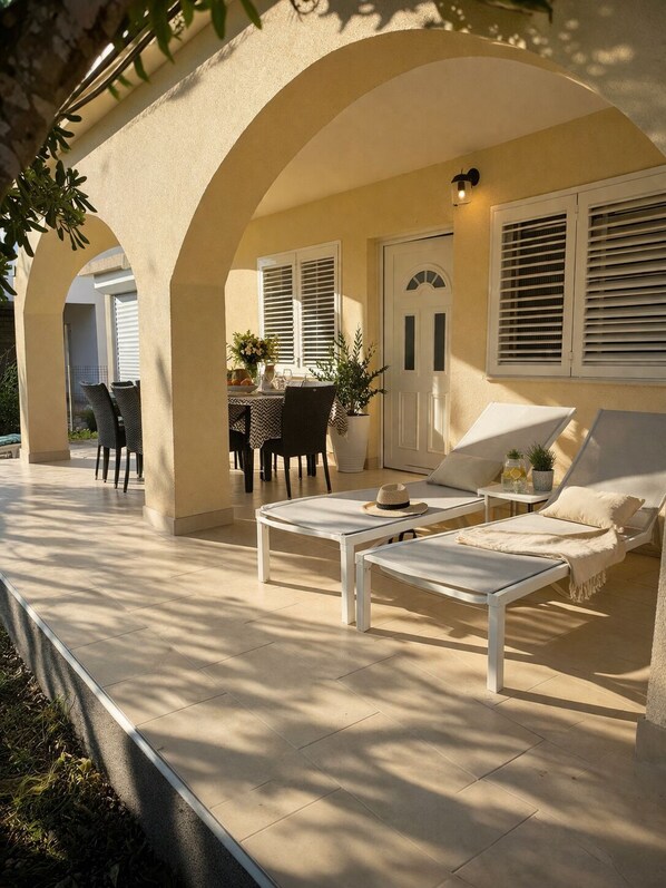 Un patio exterior con una mesa y sillas, una silla de descanso y una puerta con persianas.