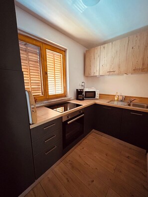 A modern kitchen with dark cabinets, a wooden countertop, a built-in oven, a microwave, and a window with blinds.