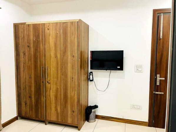 A room with a wooden wardrobe, a mounted flat-screen TV, and a door with a handle. - Hotel Noor Inn By GRB (Karnal)