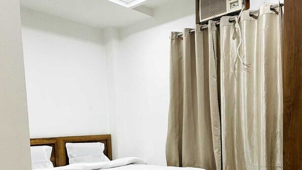 Un dormitorio con una cama, ventilador de techo, aire acondicionado y cortinas color beige.