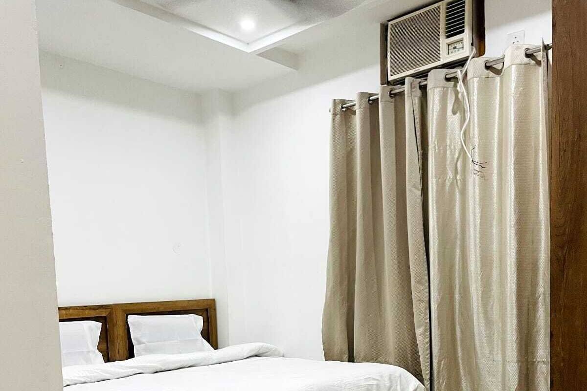 Ein Schlafzimmer mit Bett, Deckenventilator, Klimaanlage und cremefarbenen Vorhängen.