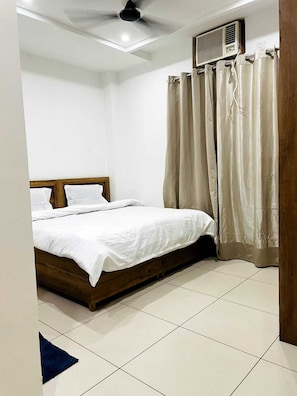 A bedroom with a bed, a ceiling fan, an air conditioning unit, and beige curtains. - Hotel Noor Inn By GRB (Karnal)