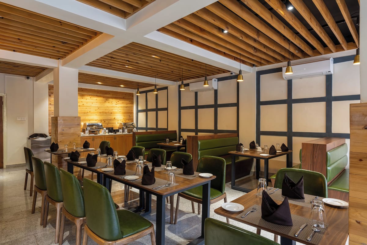 A restaurant with wooden ceiling beams, green upholstered booths, and tables set with cutlery and napkins.