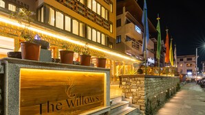 A hotel entrance with a stone facade, a wooden signboard, and potted plants. - The Willows (Thimphu)