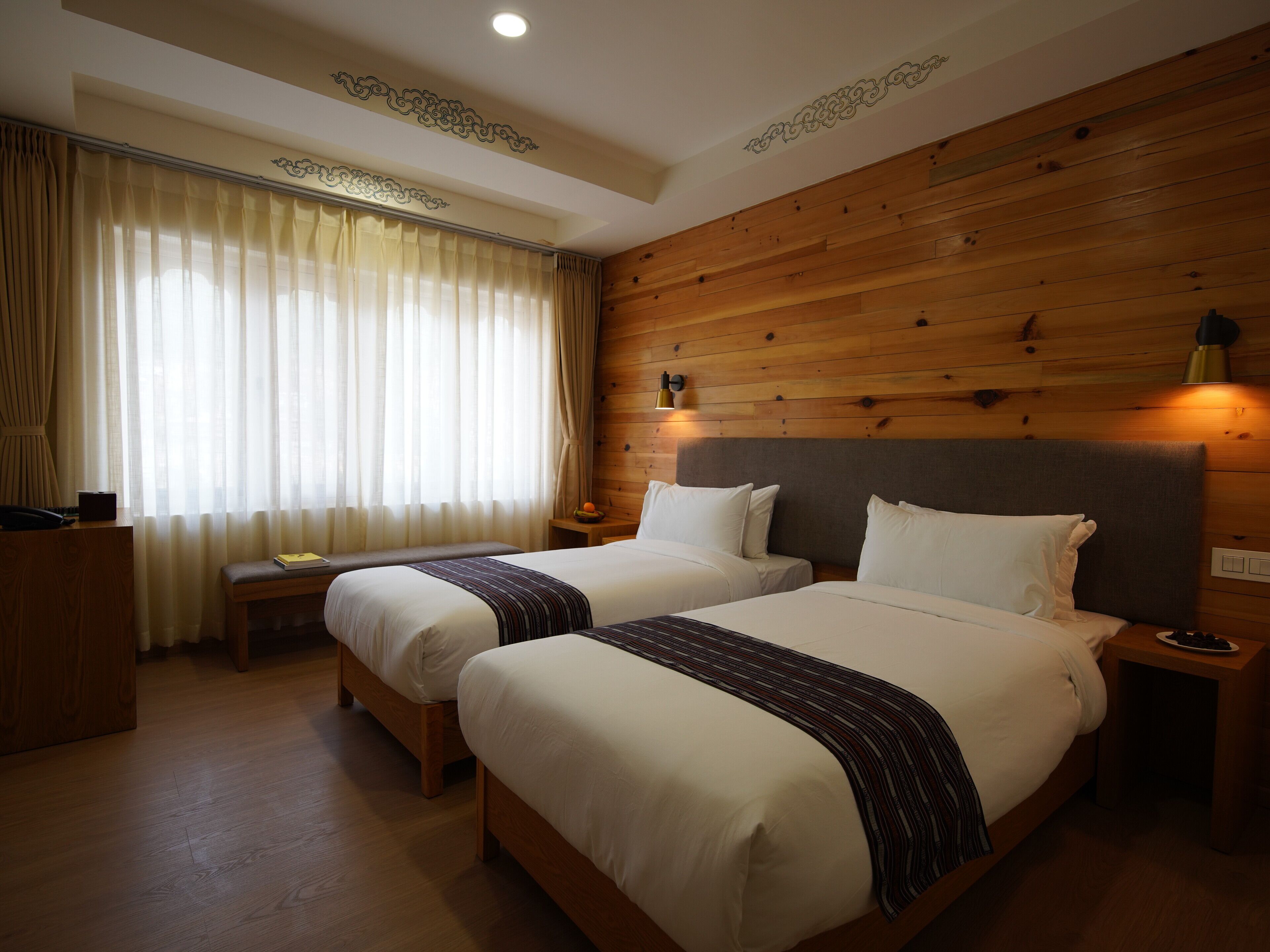 Una camera d'albergo con due letti, pannelli di legno sulle pareti, una scrivania e una finestra con tende.