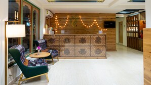 A reception area with a wooden reception desk, patterned wall, and a seating area with colorful chairs and a table. - The Willows (Thimphu)