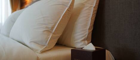 A neatly made bed with white pillows and a tissue box labeled "The Willow Hotel" on a wooden nightstand.