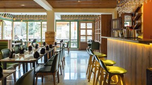 A restaurant with a long counter, multiple bar stools, and a bar area with glasses hanging above. - The Willows (Thimphu)