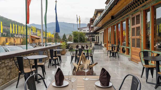 An outdoor dining area with tables and chairs, a fire pit, and flags. - The Willows (Thimphu)