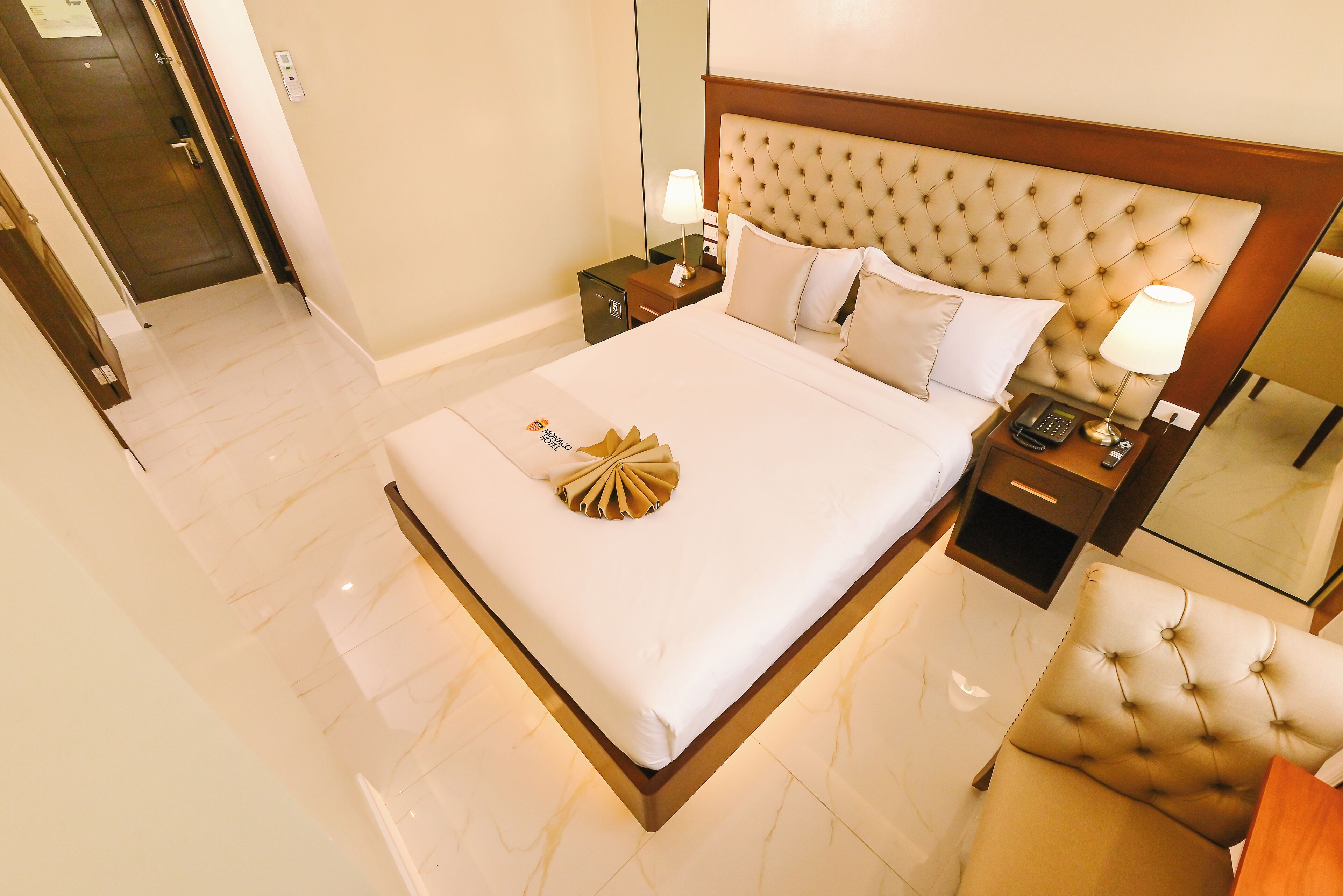 A hotel room with a large bed, a bedside table with a lamp, a bedside phone, and a chair.