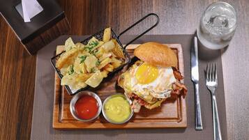 Un plato con un sándwich, un huevo frito, papas fritas y dos salsas para mojar, sobre una tabla de madera.
