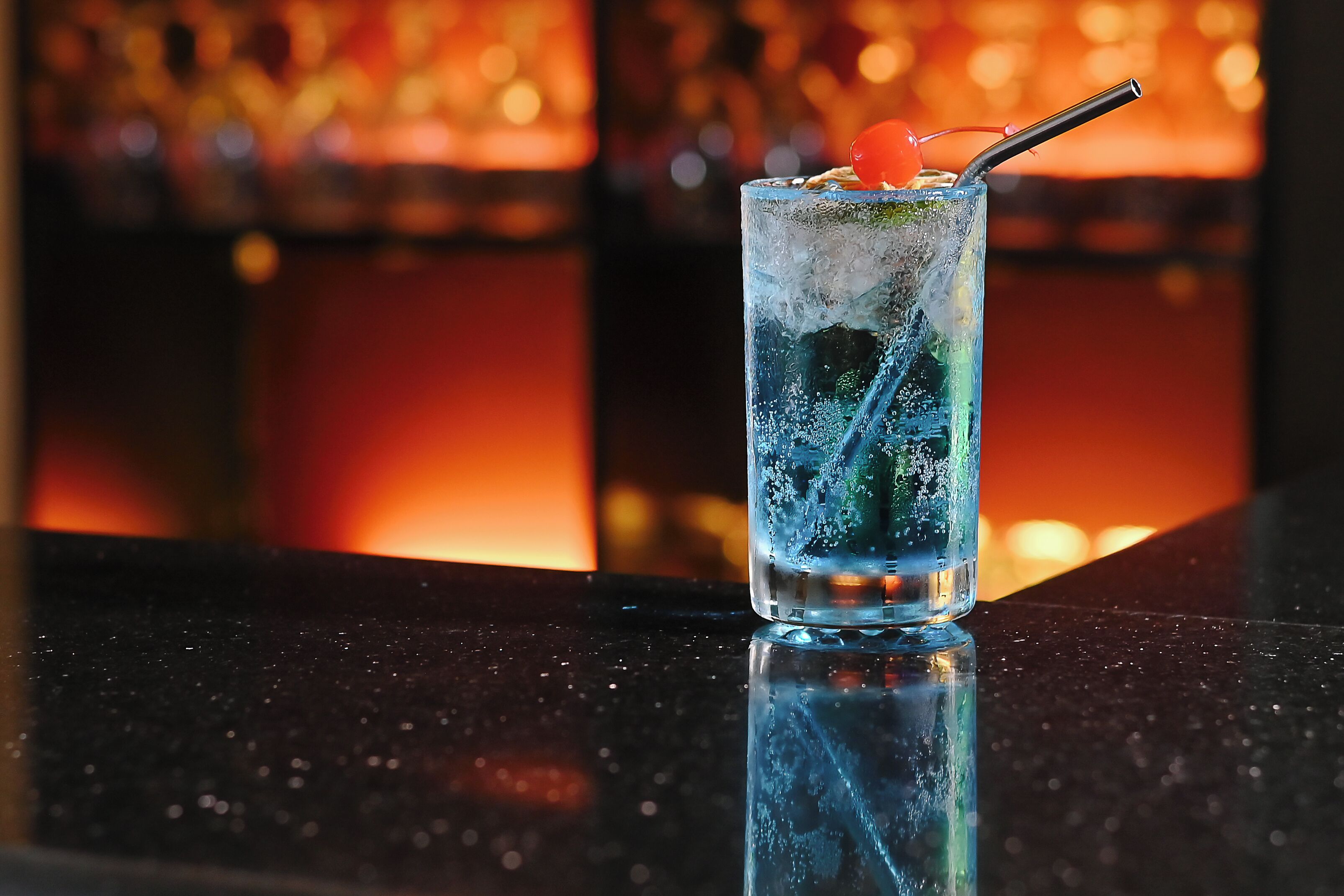 A tall glass with a straw and cherry garnish on a reflective surface.
