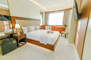 Habitación de hotel con una cama grande, mesitas de noche, un escritorio, una silla, un televisor montado en la pared y un minibar.
