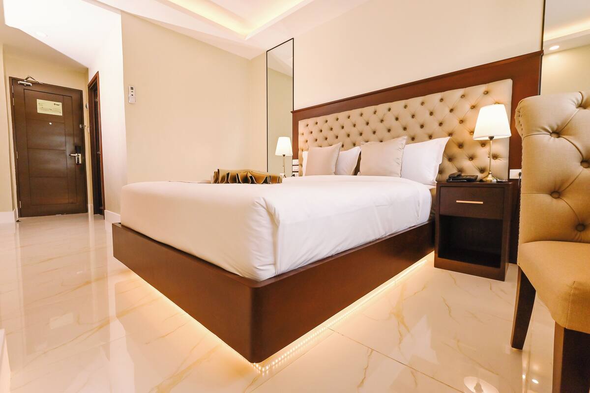 A hotel room with a large bed, a nightstand with a lamp, a chair, and a door.