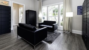 A modern hotel room with a dark leather sofa, a black storage unit, and a view of greenery through large windows. - Luxury Apt Disney-Universal-Seaworld-Conventions (Orlando)