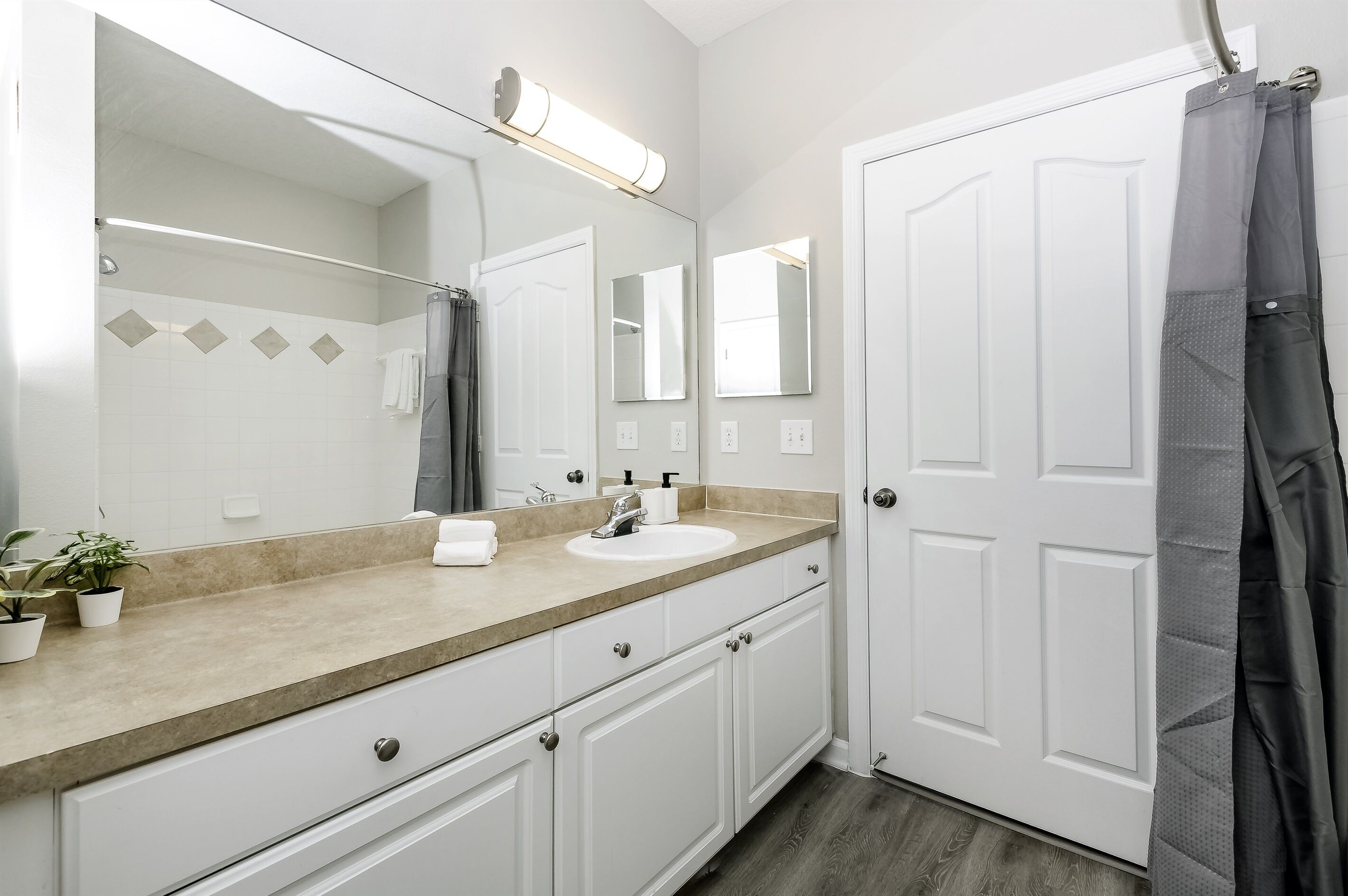 Une salle de bain avec un lavabo blanc, un grand miroir, un porte-serviettes et un rideau de douche.