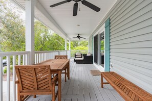 A covered porch with a wooden table and chairs, a bench, and a ceiling fan.