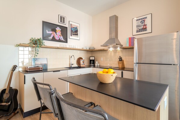 A modern kitchen with a central island, stainless steel appliances, and a guitar.