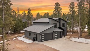 A modern two-story house with a garage, surrounded by trees and a dirt driveway. - Crescent Moon Retreat (Lead)