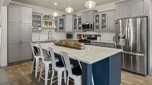 A modern kitchen with grey cabinets, a stainless steel refrigerator, a central island with bar stools, pendant lighting, and a microwave. - Crescent Moon Retreat (Lead)