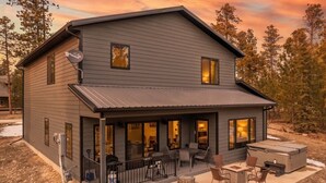 A two-story house with a covered porch, outdoor seating, and a large window overlooking a wooded area. - Crescent Moon Retreat (Lead)