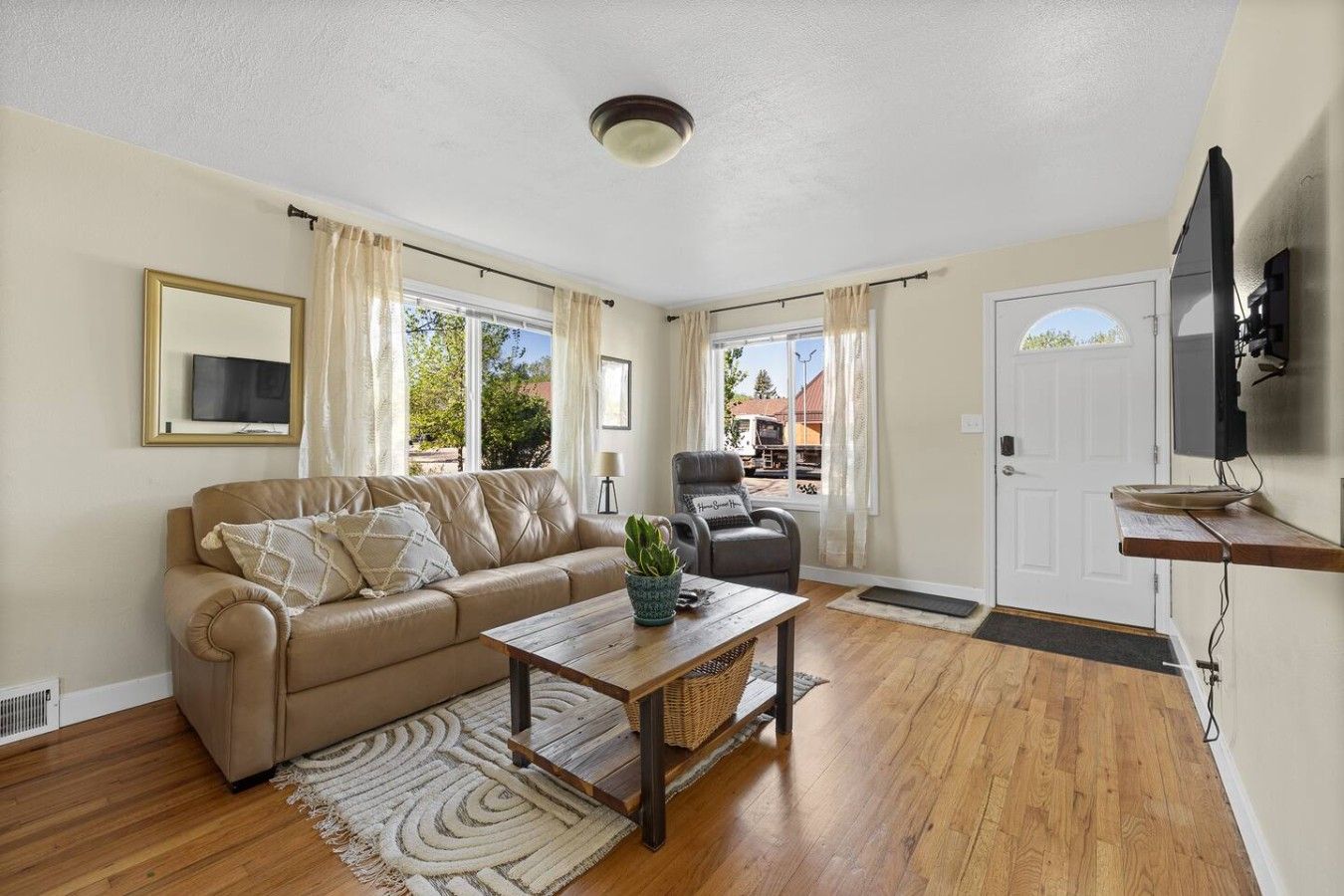 A living room with a sofa, armchair, coffee table, and a television mounted on the wall.