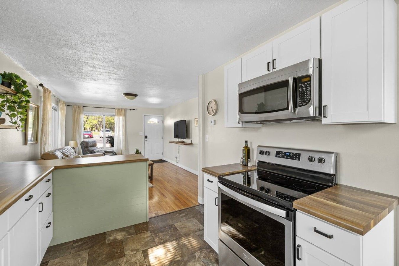 A compact kitchen with white cabinets, a microwave, a stove, and a small island with a sink.