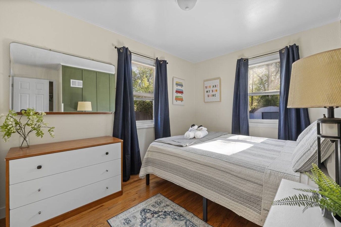 A bedroom with a bed, a dresser, a lamp, and a window with curtains.
