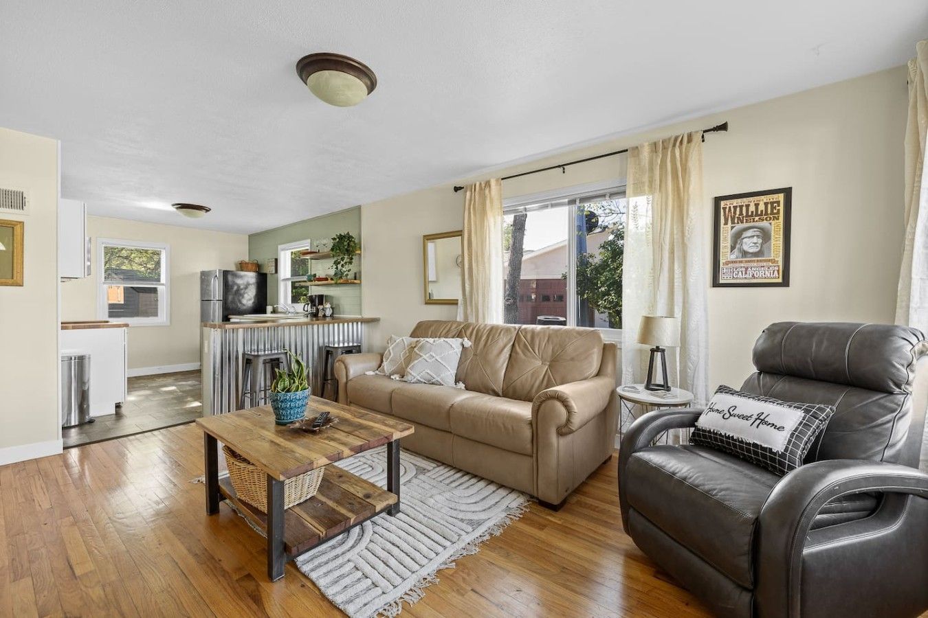 A living room with a sofa, a coffee table, a leather armchair, and a kitchen in the background.