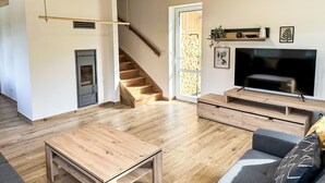 A spacious living area with wooden flooring, a staircase, a fireplace, a TV, and a sofa.