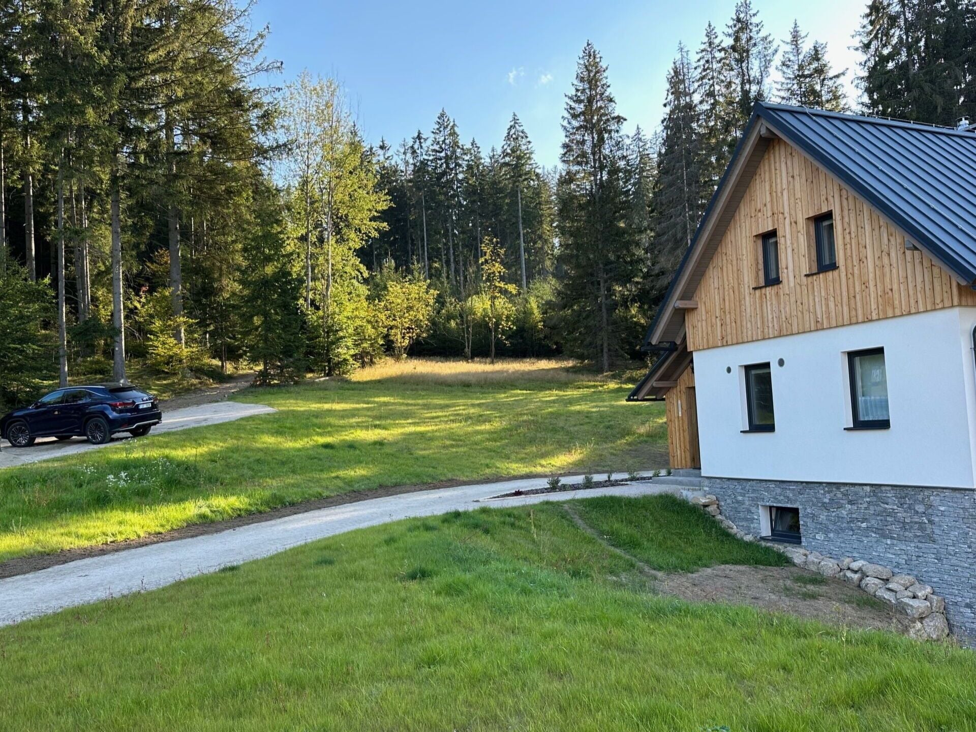 Una casa moderna con tetto spiovente, rivestimento in legno e vialetto lastricato che conduce a un'auto parcheggiata lateralmente.