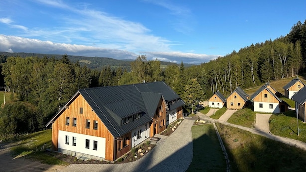 A row of wooden cabins with a gravel driveway and a forested backdrop.