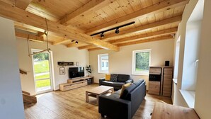 A spacious living room with wooden flooring, a black sofa, a coffee table, and a TV on a wooden stand.