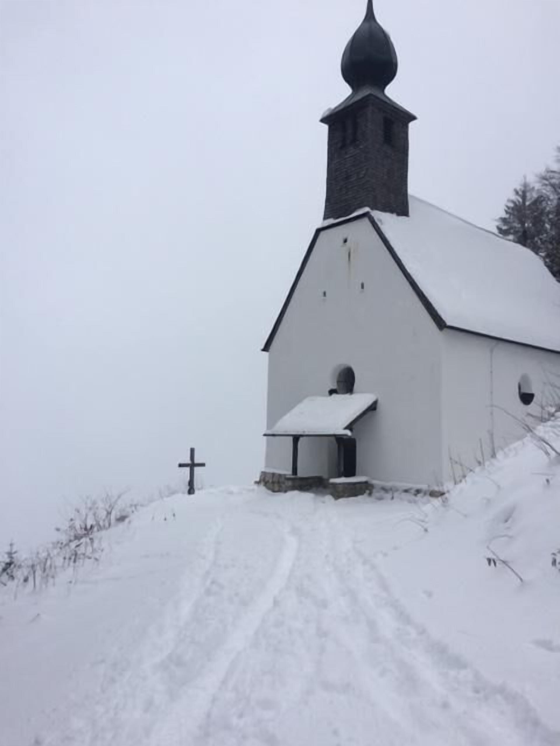 Eine schneebedeckte Kirche mit einem Kreuz voran.