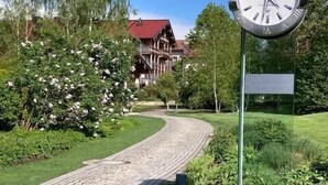 Eine Uhr mit römischen Ziffern und ein Holzbauten im Hintergrund.