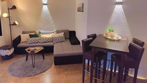 Ein modernes Wohnzimmer mit einer Couch, einem Couchtisch und einem Esstisch. Zwei Pendelleuchten befinden sich über der Couch und dem Tisch.